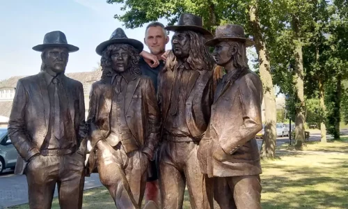 Optinet medewerker Martin poseert naast een standbeeld van vier figuren in een park.